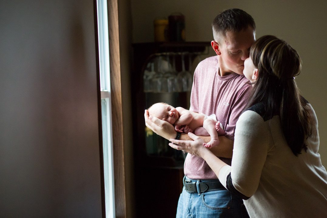 mom and dad kissing newborn in home session