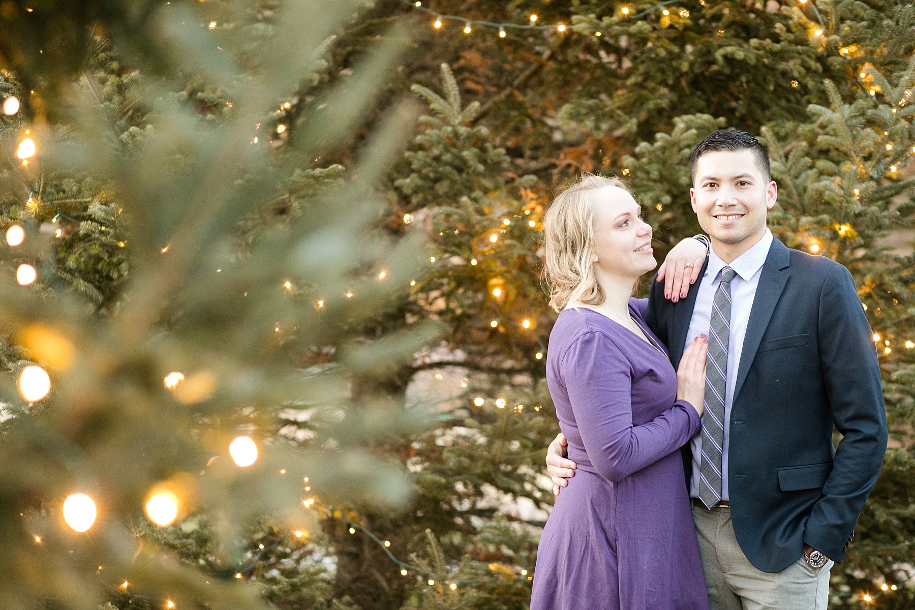 Couple in pine trees with Christmas lights.