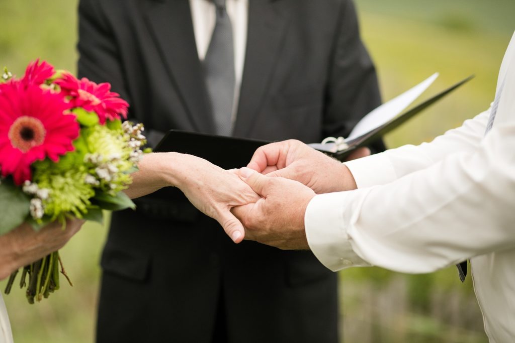 groom placing the ring on the brides hand with her bouquet