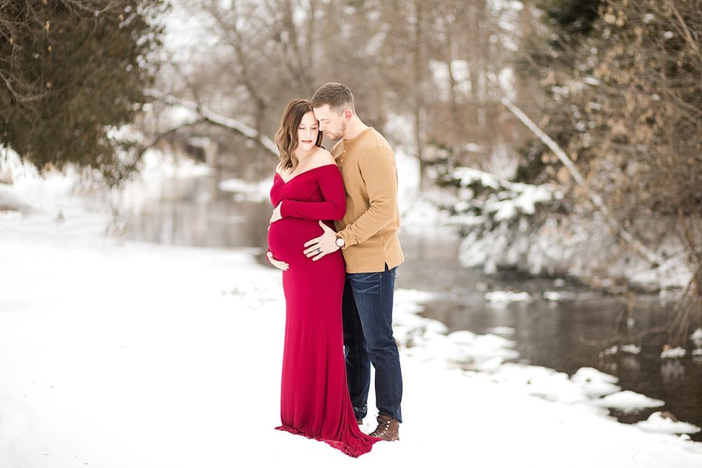 couple in the snow with a red dress on for their Eau Claire winter maternity photos