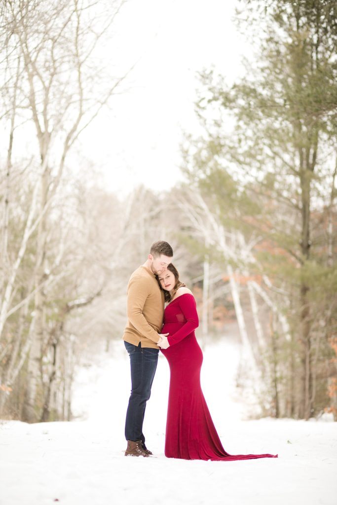 husband and wife hugging on a snow covered road for their maternity photos