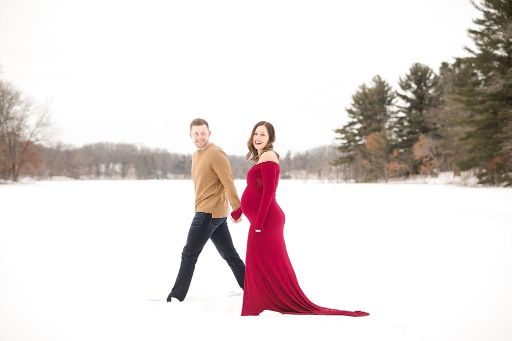 couple smiling and laughing walking across a frozen lake for their Eau Claire winter maternity photos