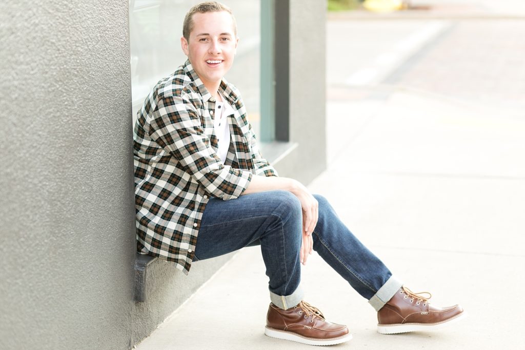 boy sitting in the windowsill of a black building for his senior photos in Eau Claire, WI