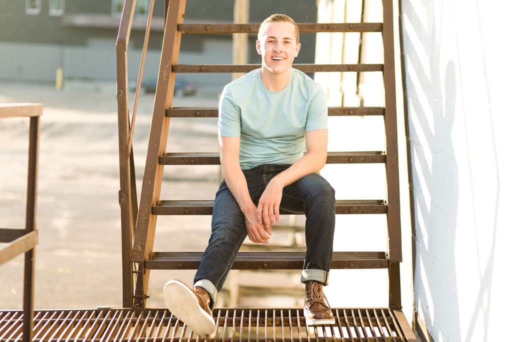 boy sitting on a rusted metal staircase in Eau Claire for his senior pictures