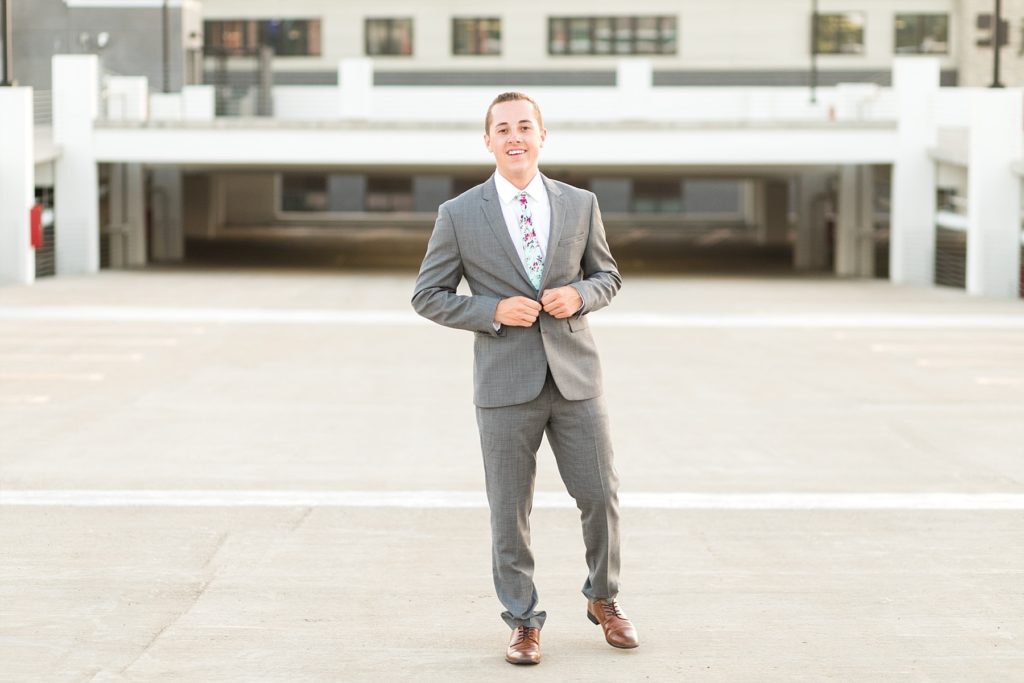 boy smiles while buttoning his suit jacket on a rooftop for his wisconsin senior pictures