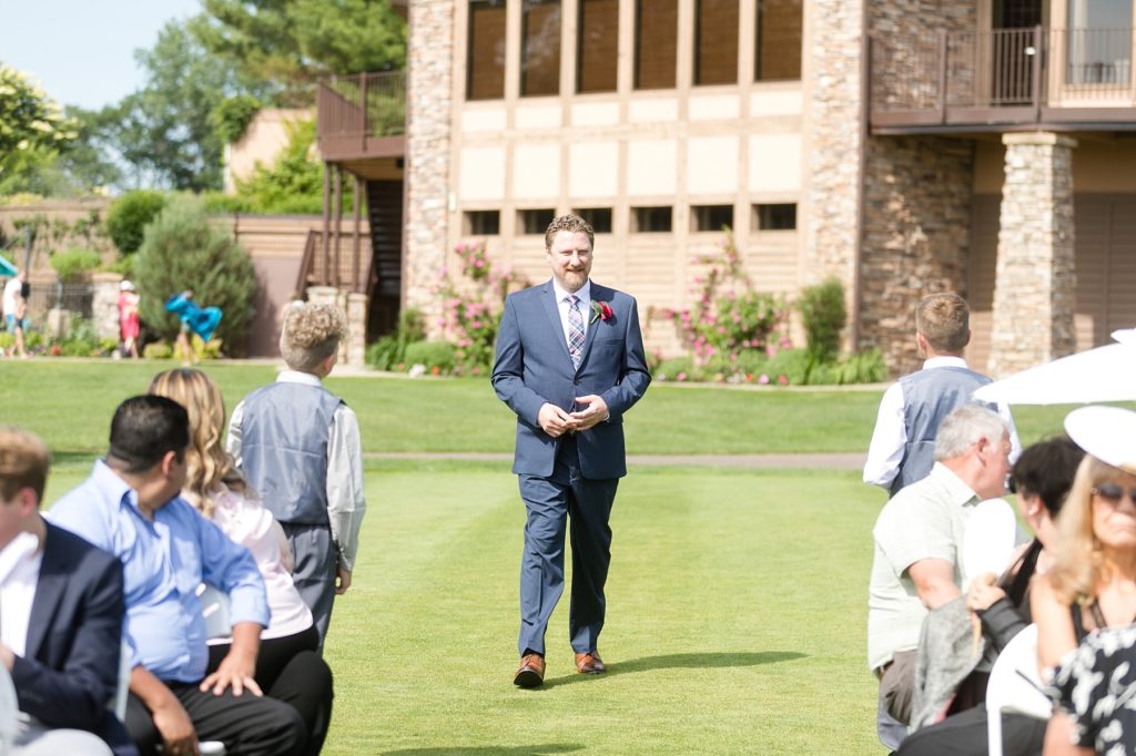 groom walking down the aisle in a navy suit at the Eau Claire Golf & Country Club