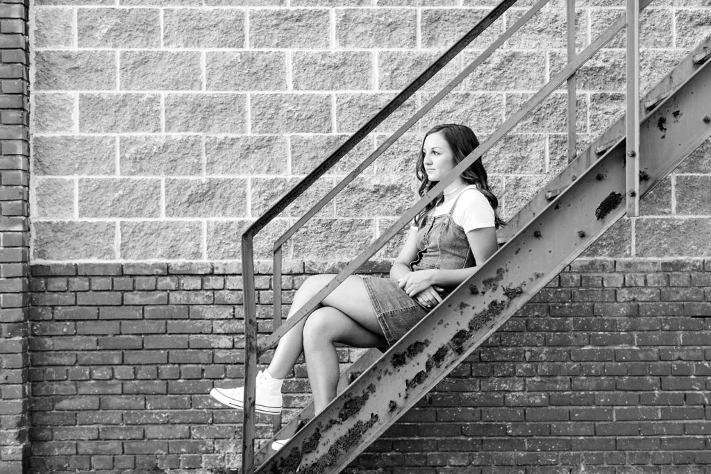 senior girl sitting on a staircase in black and white photo in eau claire