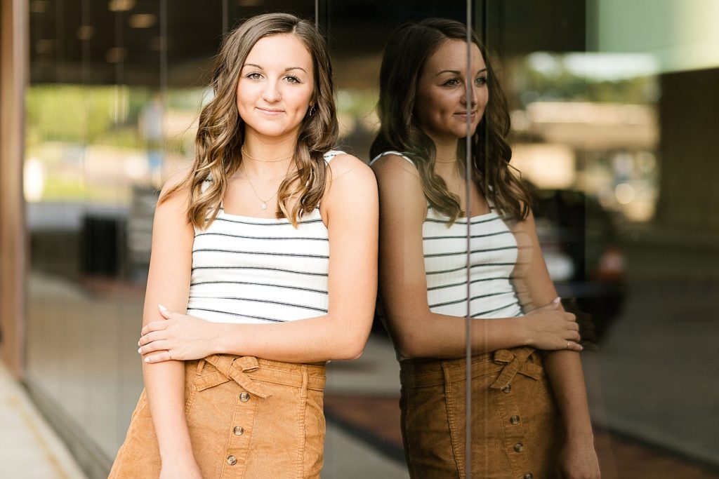 Abby leaning against a wall of windows in Eau Claire for her senior photos