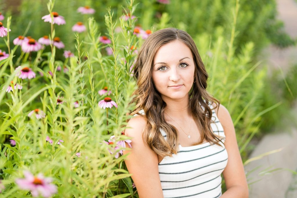 sitting in a field of pink flowers for senior photos in eau claire wi