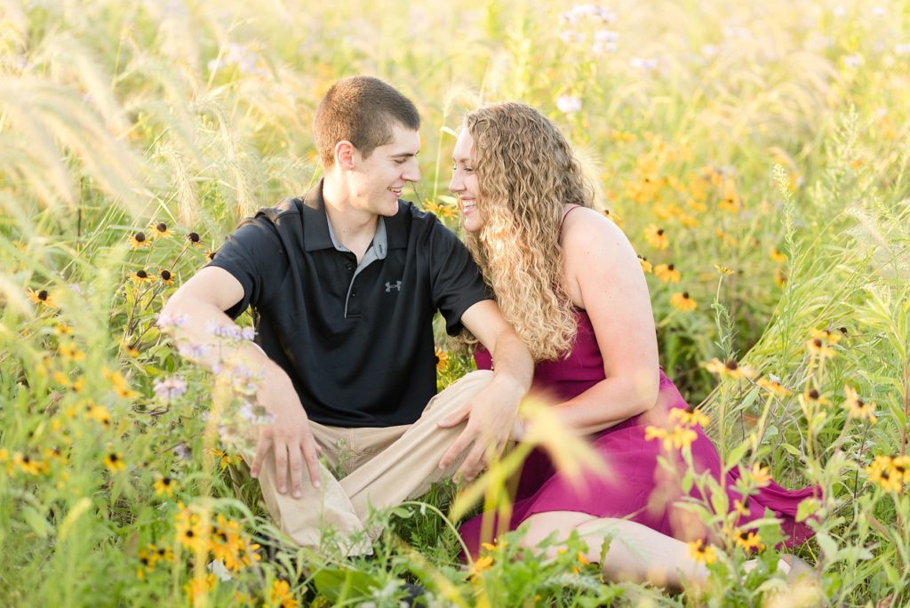couple in a field of wildflowers sitting together for their Wisconsin engagement picutres