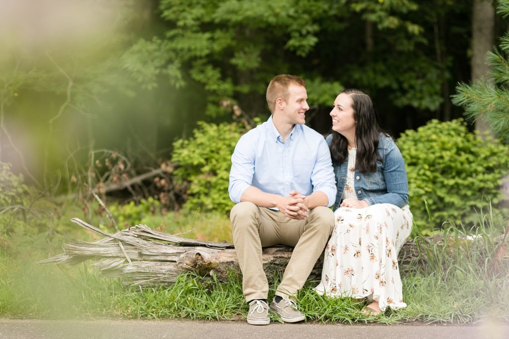 couple smiling at each other sitting on a log in Brunet Island State Park for their engagement pictures
