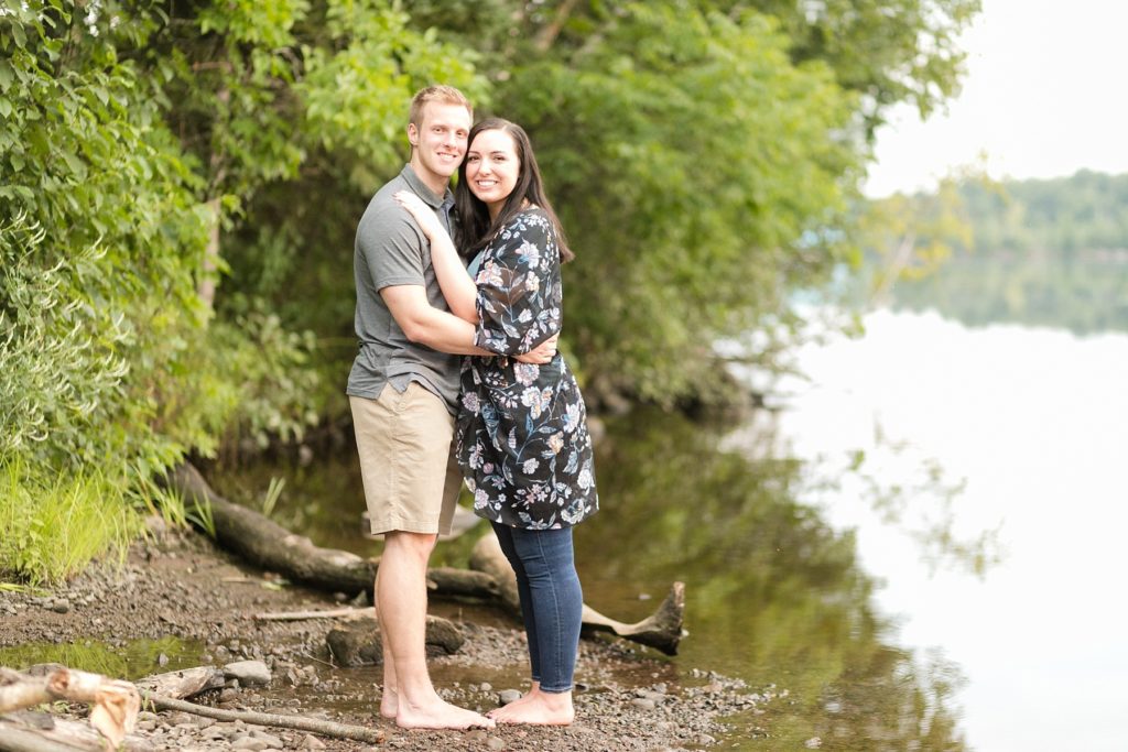 couple smiling at the camera on the shore in Brunet Island State Park for their engagement pictures