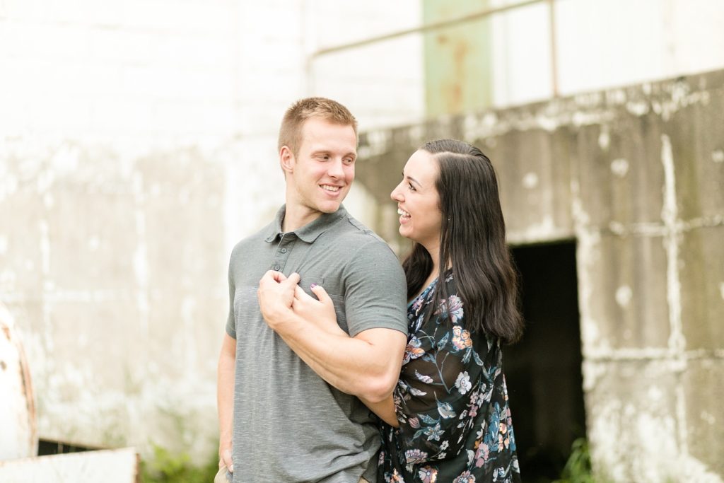 couple smiling at each other by an abandoned building  in Cornell, WI for their engagement photos