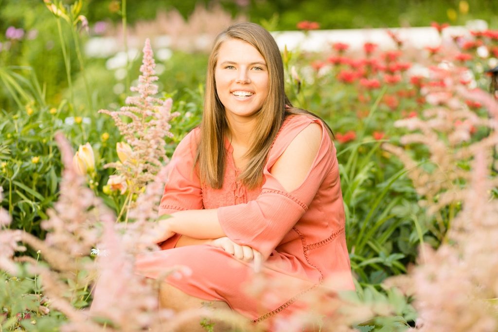 girl in a coral dress sitting in a flower garden for her senior photos in Chippewa Falls