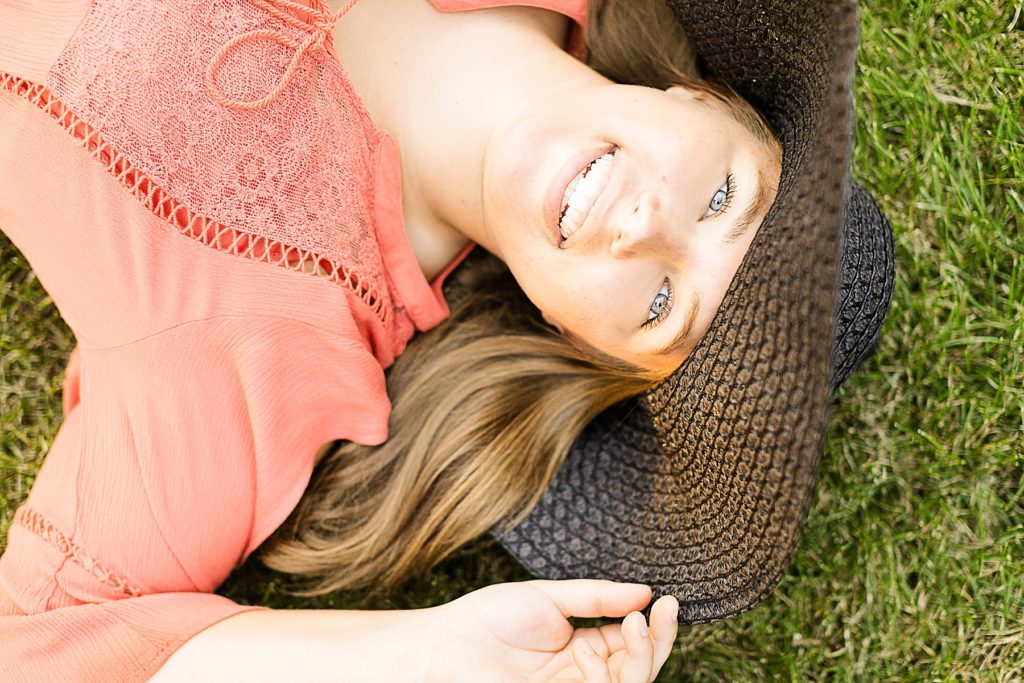 girl laying on the ground in a black hat smiling for her chippewa falls senior photos