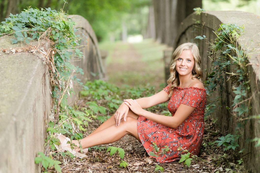 girl sitting on a vine covered abandoned bridge in Chippewa Falls for her senior photos