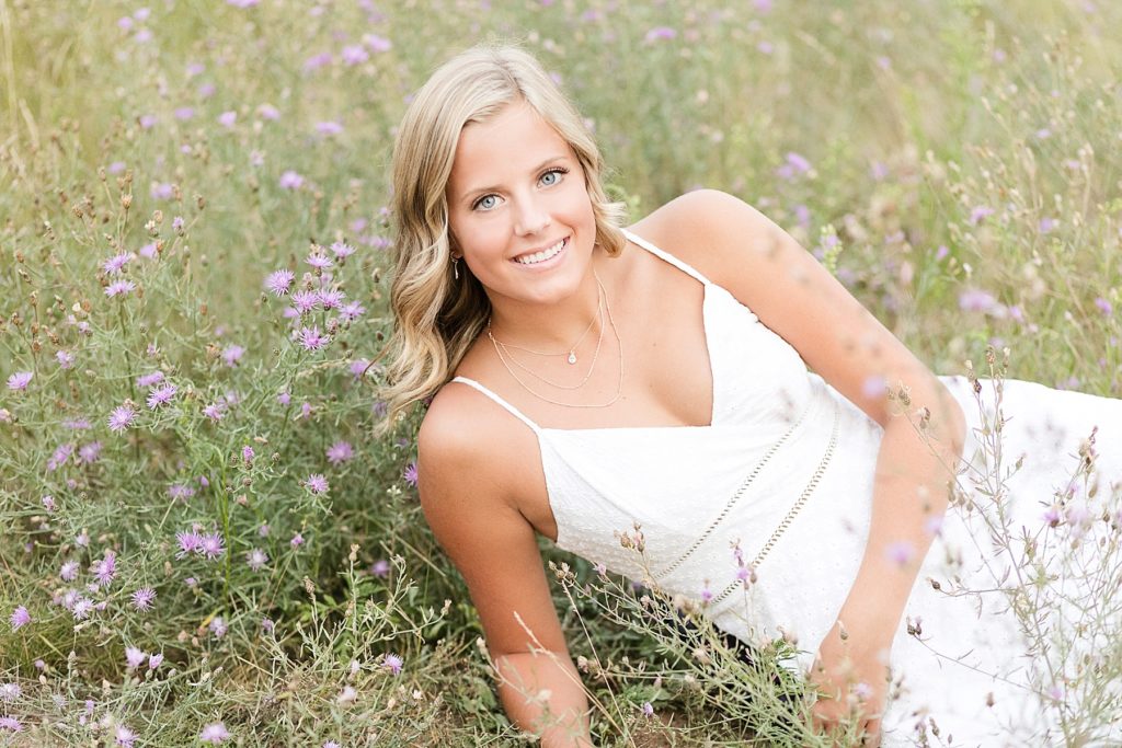 girl in laying in a field of purple flowers in a white dress in Chippewa Falls for her senior photos