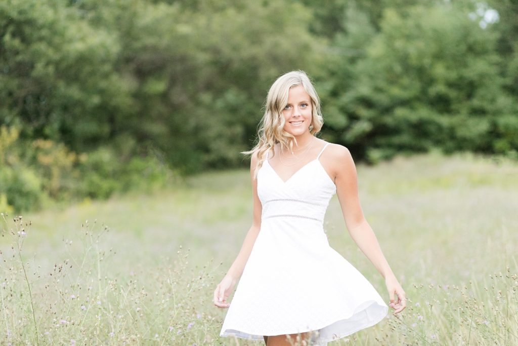 girl twirling in a field of flowers in a white dress in Chippewa Falls for her senior photos
