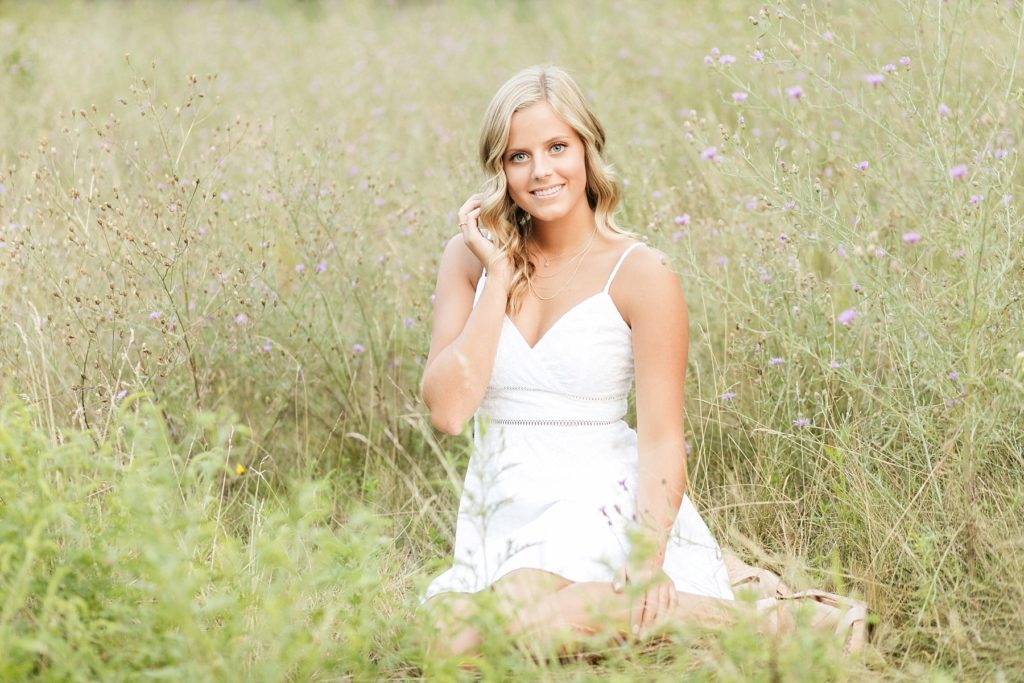 girl in a white dress sitting in a field of purple flowers and tall grass in Chippewa Falls for her senior photos