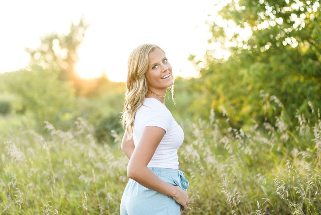 girl looking over her shoulder laughing in Wisconsin on their farm in tall grass for her senior photos