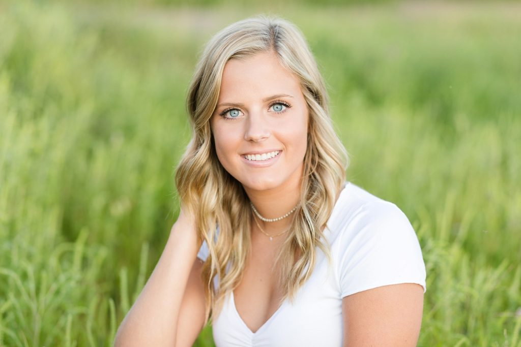 girl sitting in soft green grass smiling in a white shirt in Wisconsin for her senior photos