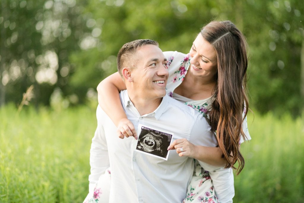 guy holding a girl on his back with an ultrasound photo for their pregnancy announcement session in Eau Claire, Wisconsin
