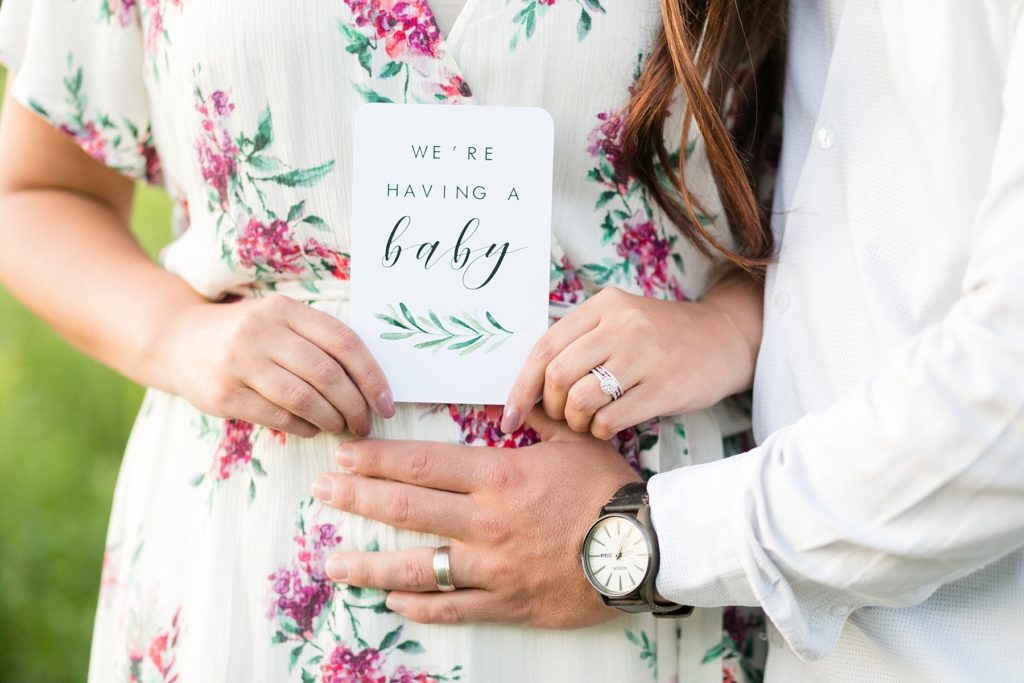 couple holding a sign that says "we're having a baby" with his hand on her belly for their pregnancy and anniversary session