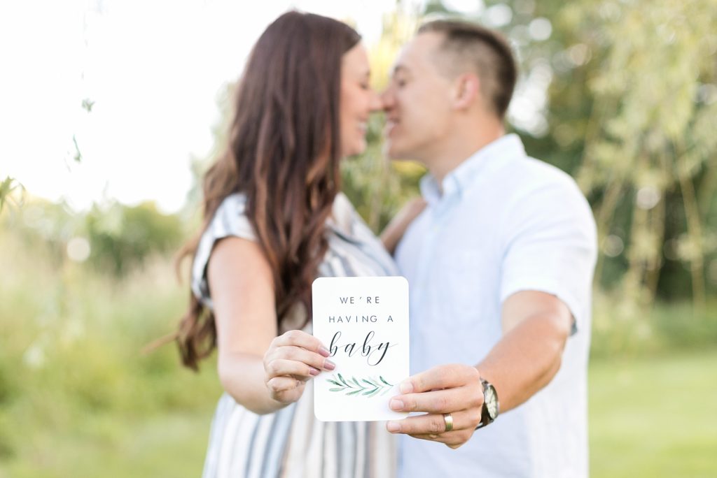 couple holding a card that reads "we're having a baby" for their Eau Claire Anniversary Session