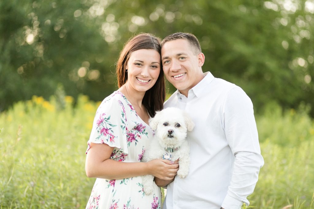 couple holding their white dog in a field for their anniversary session in Eau Claire