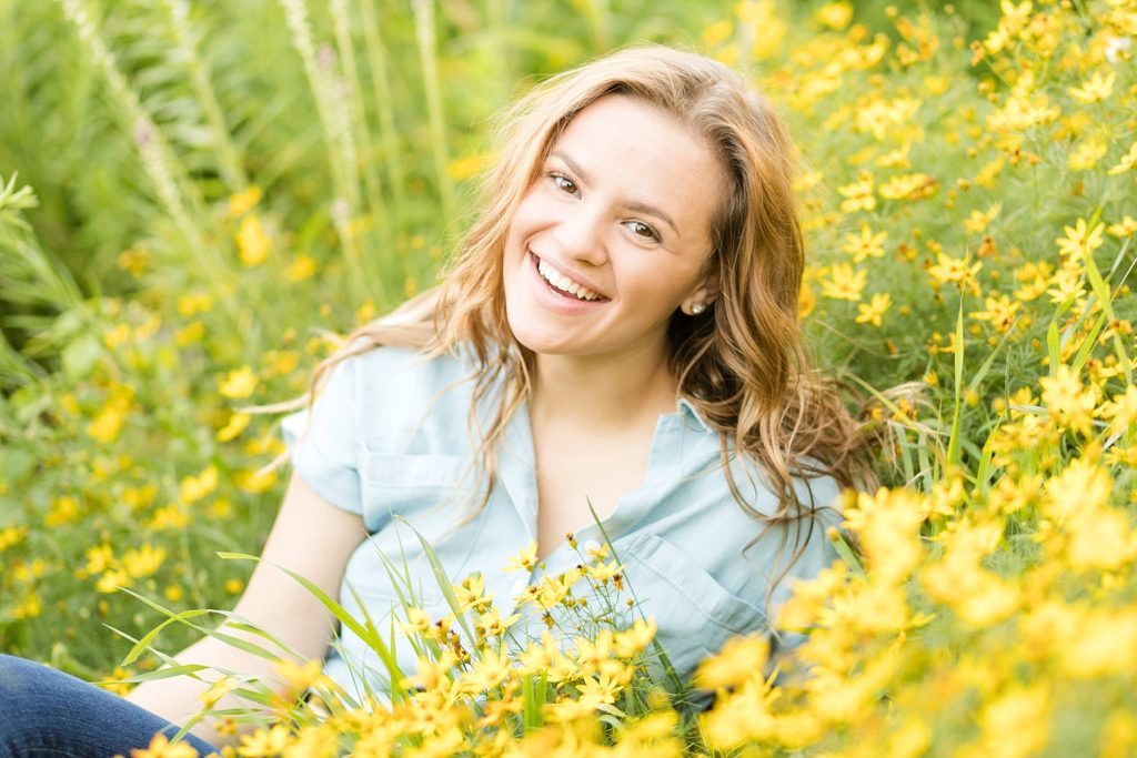 girl smiling sitting in yellow flowers with a blue shirt on for her sweet 16 photos in Eau Claire Wisconsin