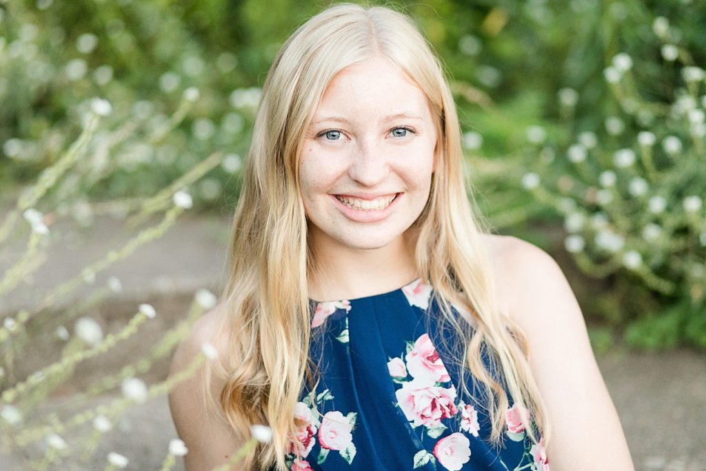 girl in blue dress sitting in white flowers smiling for her Thorp WI Senior photos