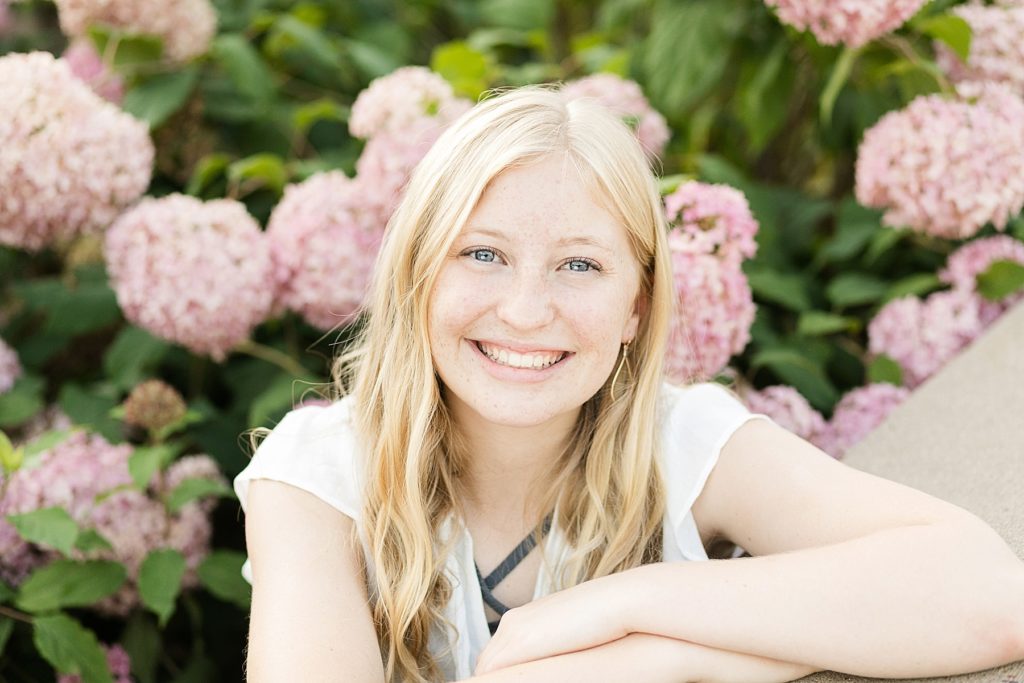 girl with blonde hair sitting in pink hydrangeas for her Thorp WI Senior photos