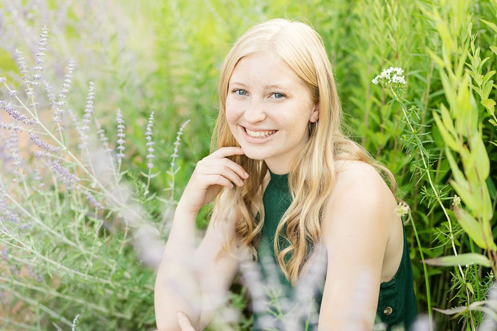 girl sitting in green grass and purple flowers for her Thorp WI Senior photos