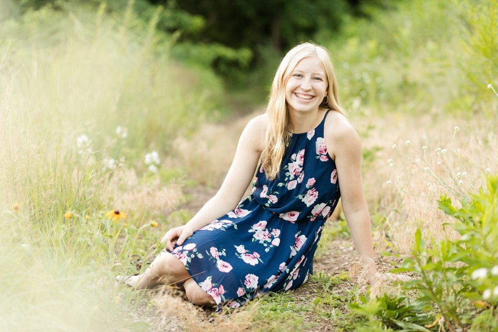girl sitting on the ground in flowers laughing for her Thorp WI Senior photos