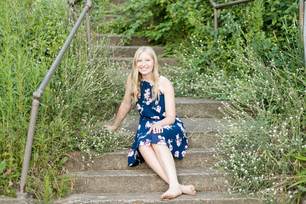 girl sitting on cement stairs with white flowers around her in a blue dress for her Thorp WI Senior photos