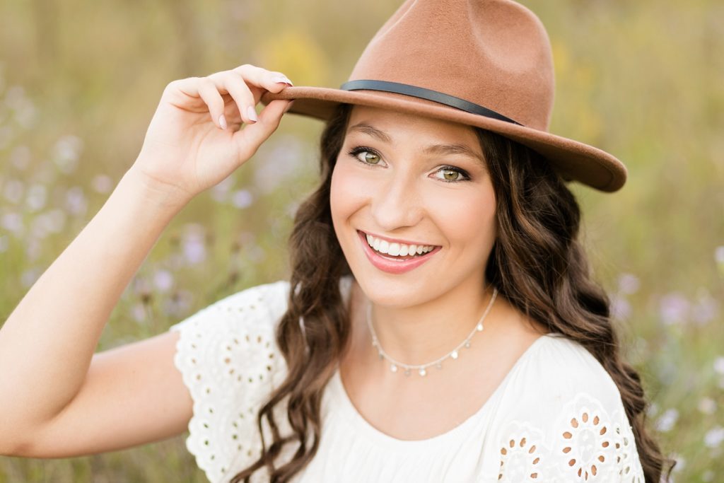 Cadott high school senior Tabitha smiles at the camera with a hat on in a field of flowers.
