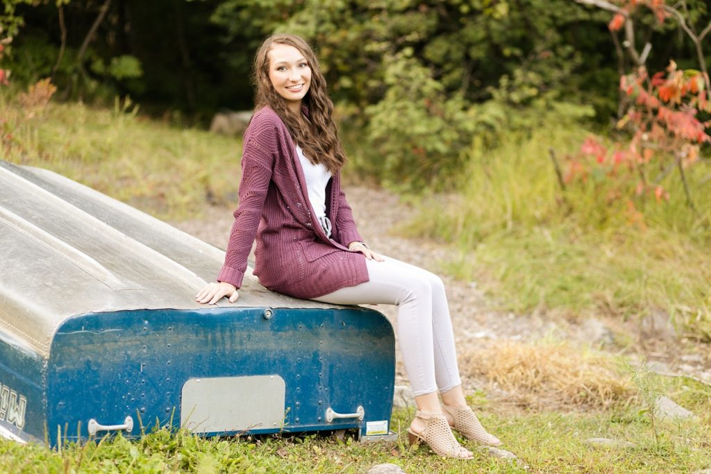 girl in a purple sweater sitting on an upturned boat with a blue back for her senior pictures at a Wisconsin state park