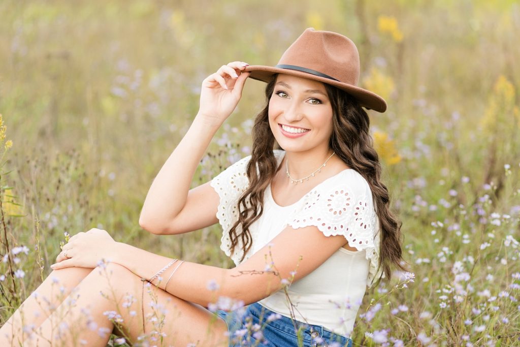 Girl in brown hat smiling at the camera for her senior photos at Lake Wissota State Park in a flower field
