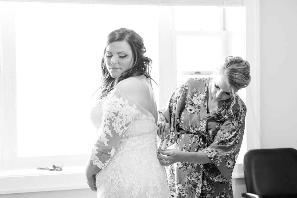 maid of honor buttoning bride into her lace gown on her wedding day at Lake Wissota Golf & Events