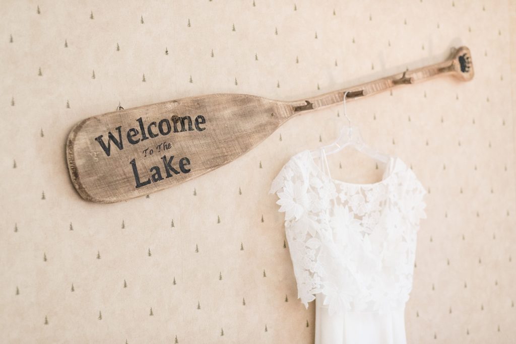 brides dress hanging from a canoe paddle that reads "welcome to the lake" at The Beacons of Minocqua on their wedding day
