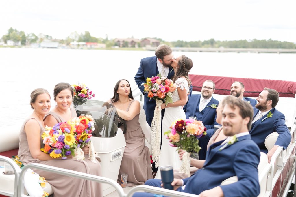 bride and groom with bridal party on a pontoon kissing on the lake at The Beacons of Minocqua on their wedding day