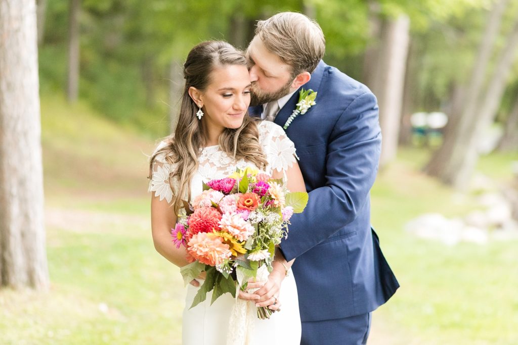 groom kissing brides cheek outside with a bright bouquet at The Beacons of Minocqua on their wedding day
