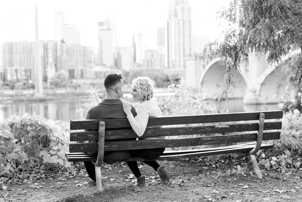 couple sitting on a bench in a black and white photo for their fall engagement session in Minneapolis at St. Anthony Main