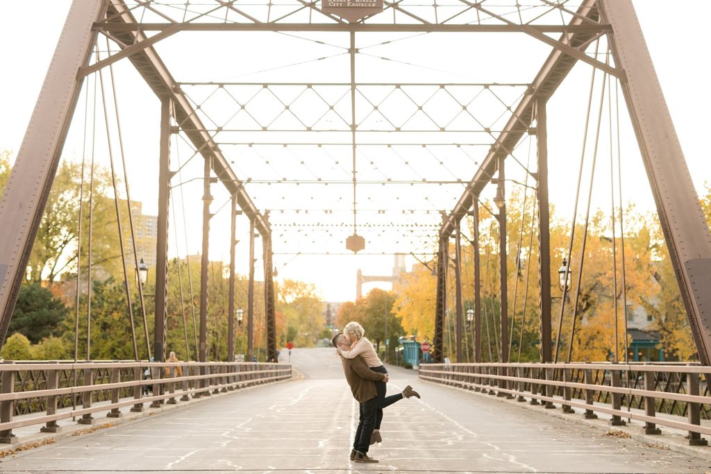 guy lifting girl up on bridge for their fall engagement session in Minneapolis at St. Anthony Main