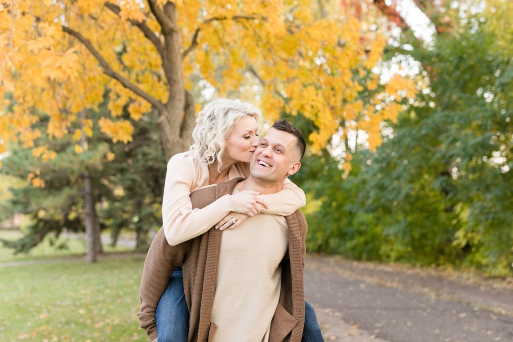 guy giving girl piggy back ride for their fall engagement session in Minneapolis at St. Anthony Main