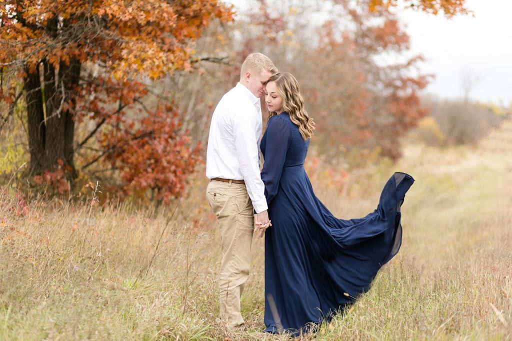 couple in a field with the wind blowing her dress from Lulus for their woodsy Wisconsin engagement session