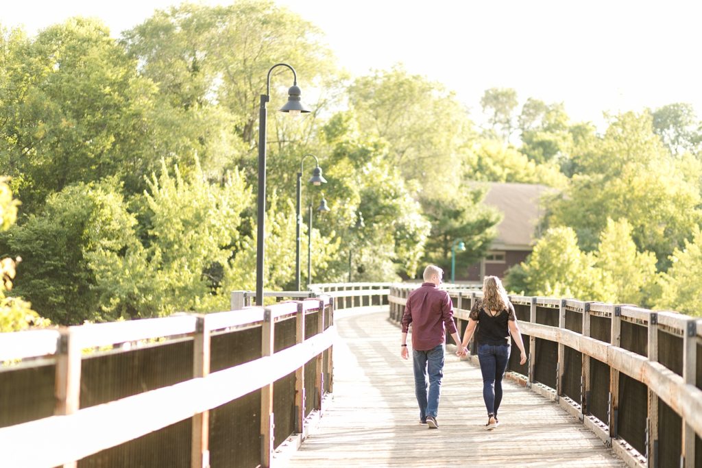 couple walking on the footbridge in Eau Claire for their engagement photos on a bright sunny day