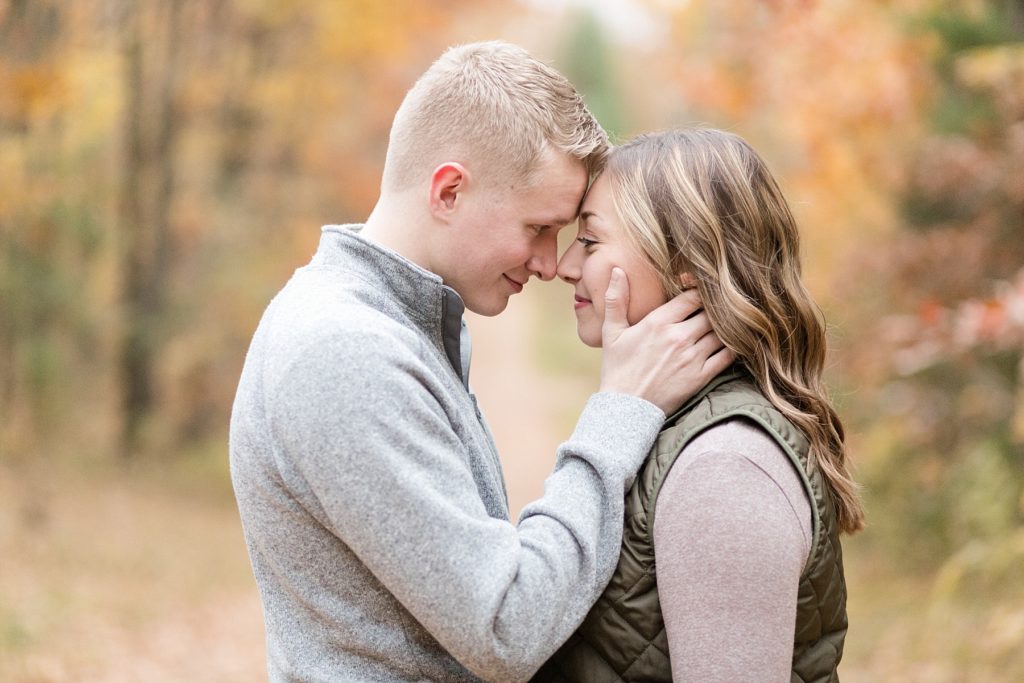 couple nose to nose on a dirt road in the fall for their woodsy Wisconsin engagement session