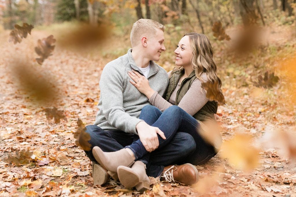 couple sitting in a pile of leaves in the fall for their woodsy Wisconsin engagement session