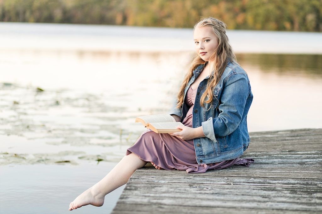 girl on dock with book for her Bloomer WI senior photos